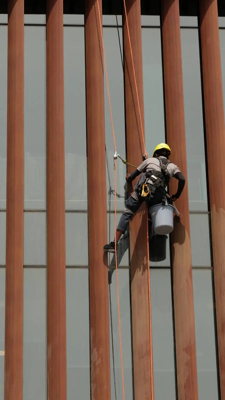 Rope access technician working across a timber-louvre facade